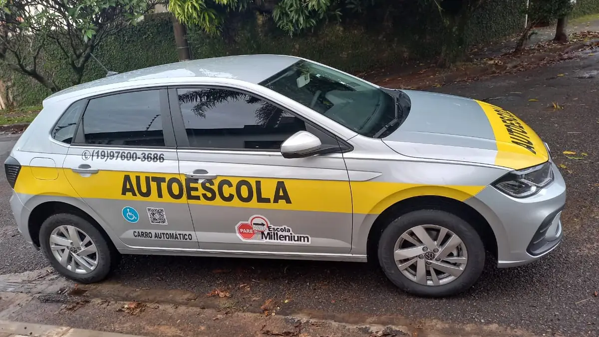 Carro automático da Millenium, um VW Polo prata adesivado com AUTOESCOLA e CARRO AUTOMÁTICO, parado na rua